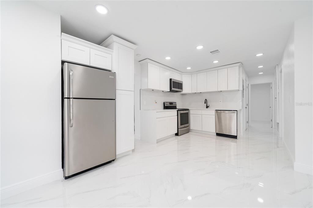 A modern kitchen features white cabinets, stainless steel appliances, and white marble-patterned tile flooring — 5621 LUNSFORD DRIVE, ORLANDO, FL