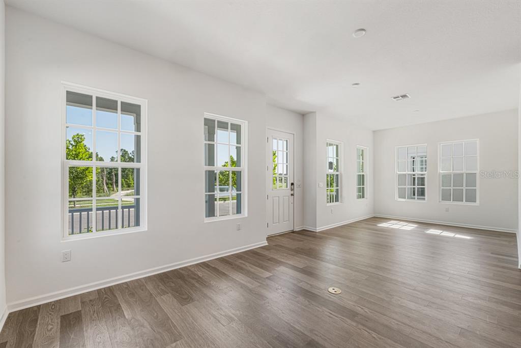 An empty room features light gray walls, wood-look flooring, and several windows with white trim — 1827 HEADLAND LOOP, KISSIMMEE, FL