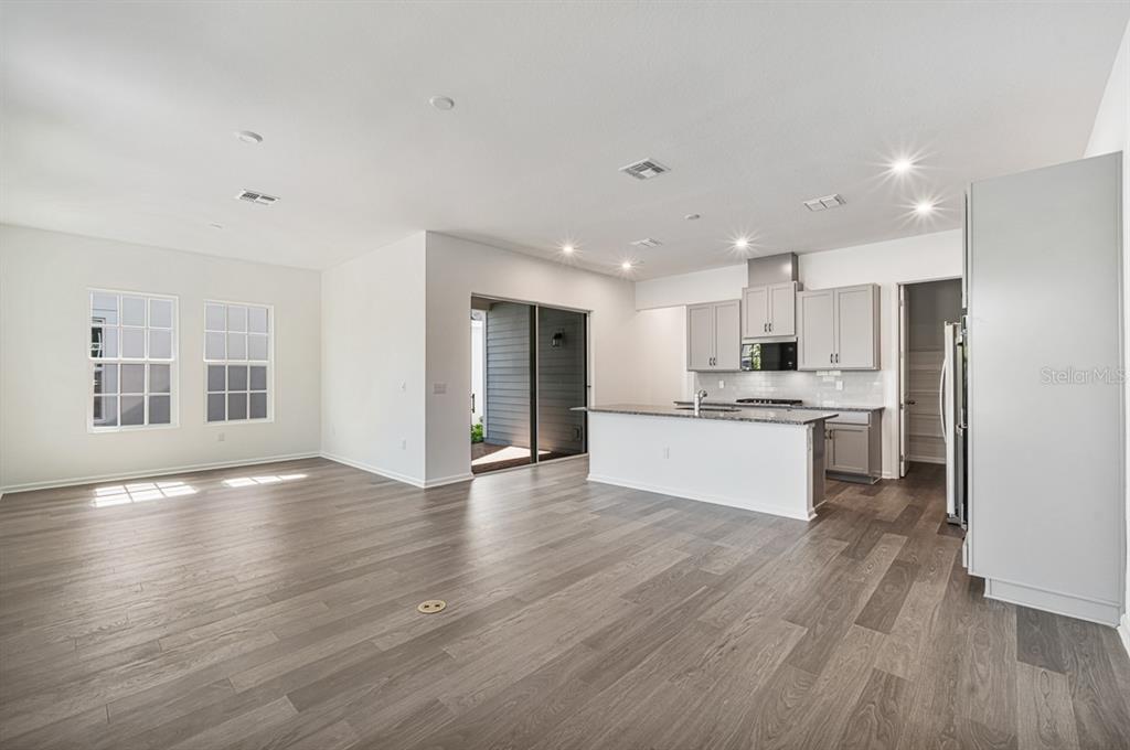 An open-concept kitchen and living area features gray cabinetry, a kitchen island, and wood flooring — 1827 HEADLAND LOOP, KISSIMMEE, FL