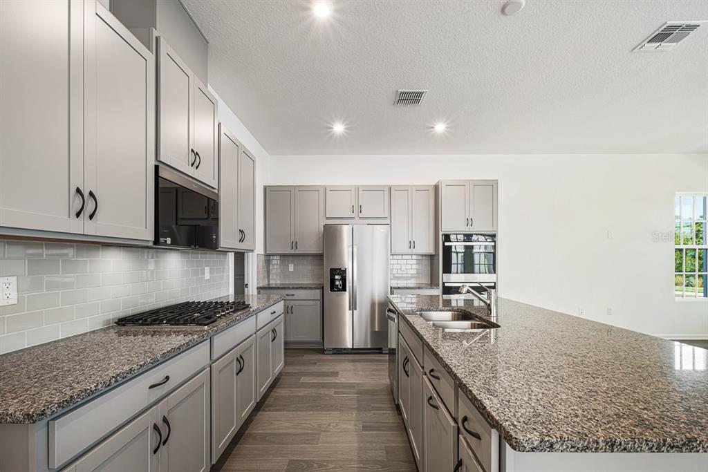 A kitchen with gray cabinets, granite countertops, stainless steel appliances, and a large center island — 1827 HEADLAND LOOP, KISSIMMEE, FL
