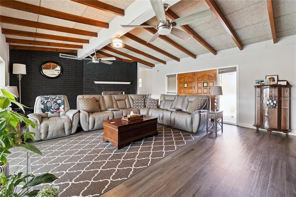 A living room features a grey sectional sofa, black brick fireplace, and exposed wood ceiling beams — 2925 E LAKE HARTRIDGE DRIVE, WINTER HAVEN, FL