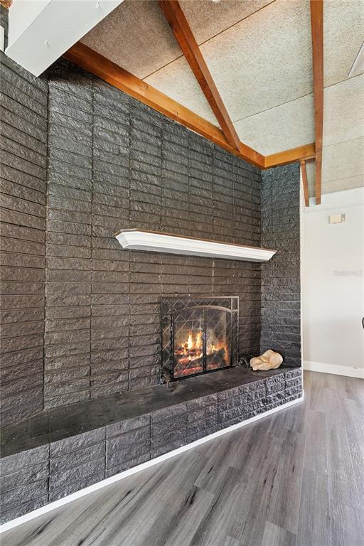 A living room features a dark textured brick fireplace with a white mantel and wood beams — 2925 E LAKE HARTRIDGE DRIVE, WINTER HAVEN, FL