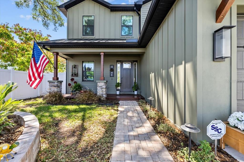 A paved walkway leads to the covered front porch of a green house with stone columns — 3804 N DARWIN AVENUE, TAMPA, FL