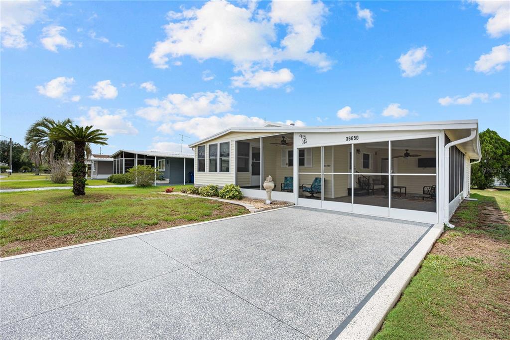 A single-story manufactured home features a screened-in front porch and a concrete driveway — 36650 DINA DRIVE, ZEPHYRHILLS, FL