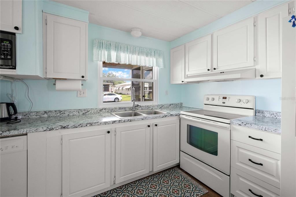 A kitchen features white cabinets, granite-look countertops, a white stove, and a window over the sink — 36650 DINA DRIVE, ZEPHYRHILLS, FL