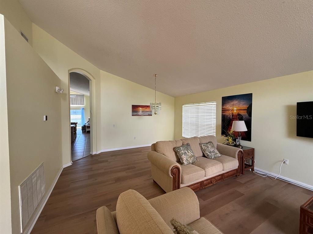 A living room features light-colored walls, wood-look flooring, a beige sofa, and a vaulted ceiling — 318 LANGHAM DRIVE, DAVENPORT, FL