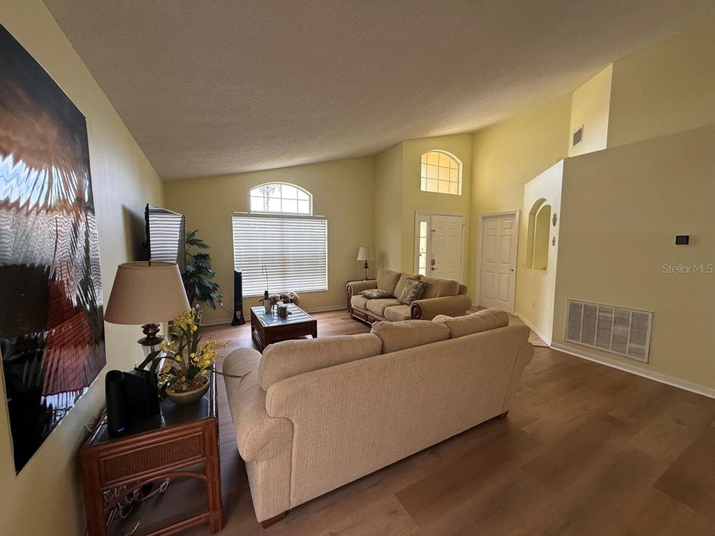 A living room features light-colored walls, wood-look flooring, two beige sofas, and a vaulted ceiling — 318 LANGHAM DRIVE, DAVENPORT, FL