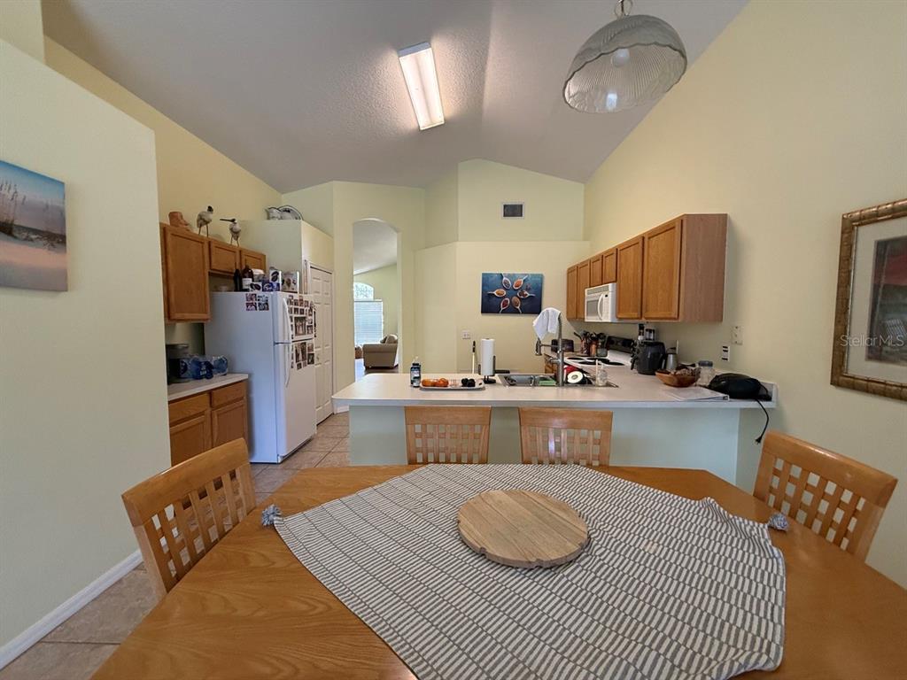A kitchen with wood cabinets, white appliances, and a breakfast bar overlooks a dining area — 318 LANGHAM DRIVE, DAVENPORT, FL