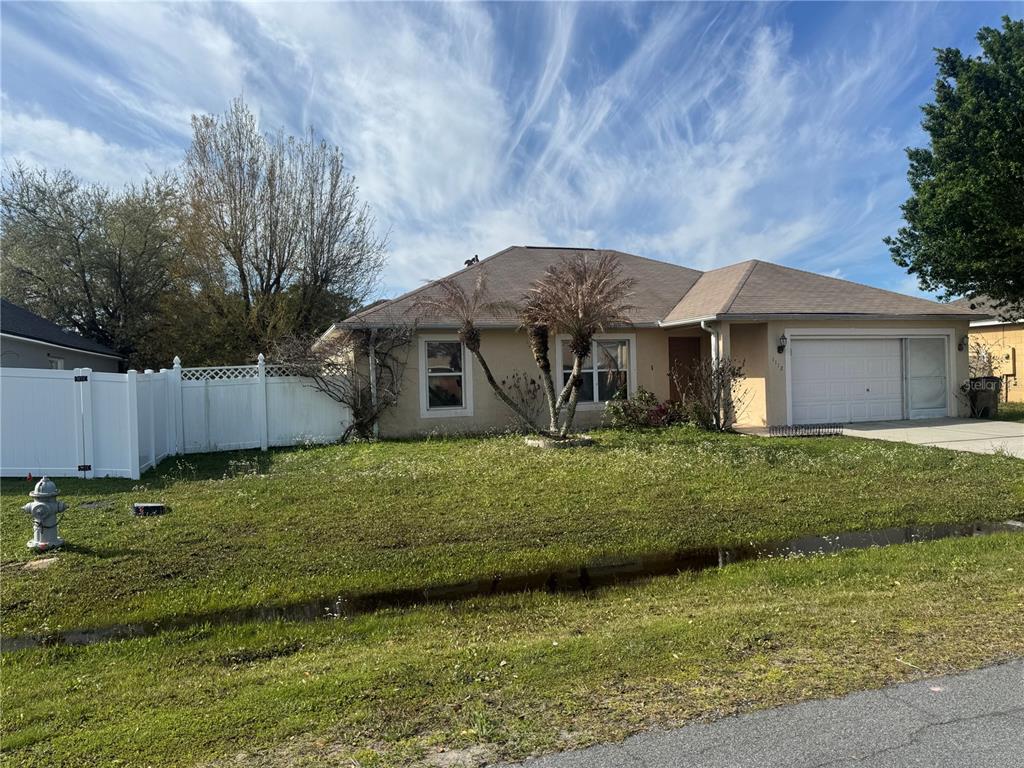 A single-story house with a tan exterior, a two-car garage, and a white vinyl fence — 1112 ROAN COURT, KISSIMMEE, FL