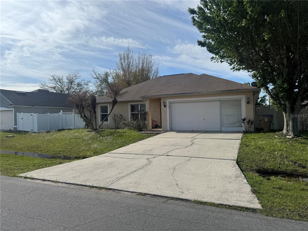 A single-story house with a beige stucco exterior, a two-car garage, and a concrete driveway — 1112 ROAN COURT, KISSIMMEE, FL