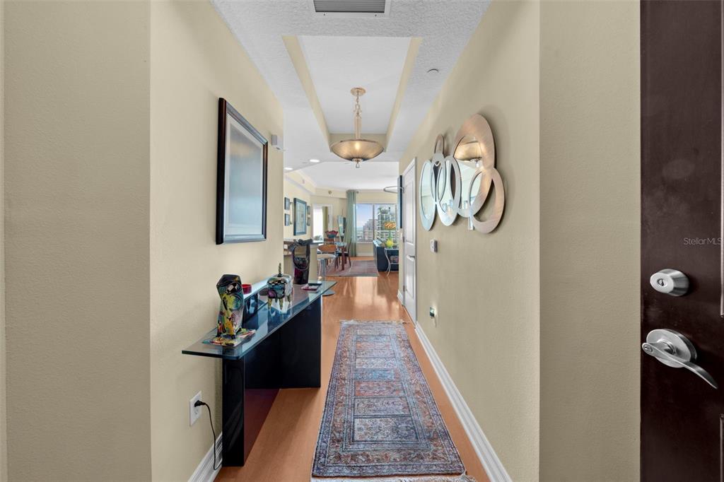 A hallway with a runner rug, console table, and wall mirrors leads to an open living area — 449 S 12TH STREET UNIT 2205, TAMPA, FL