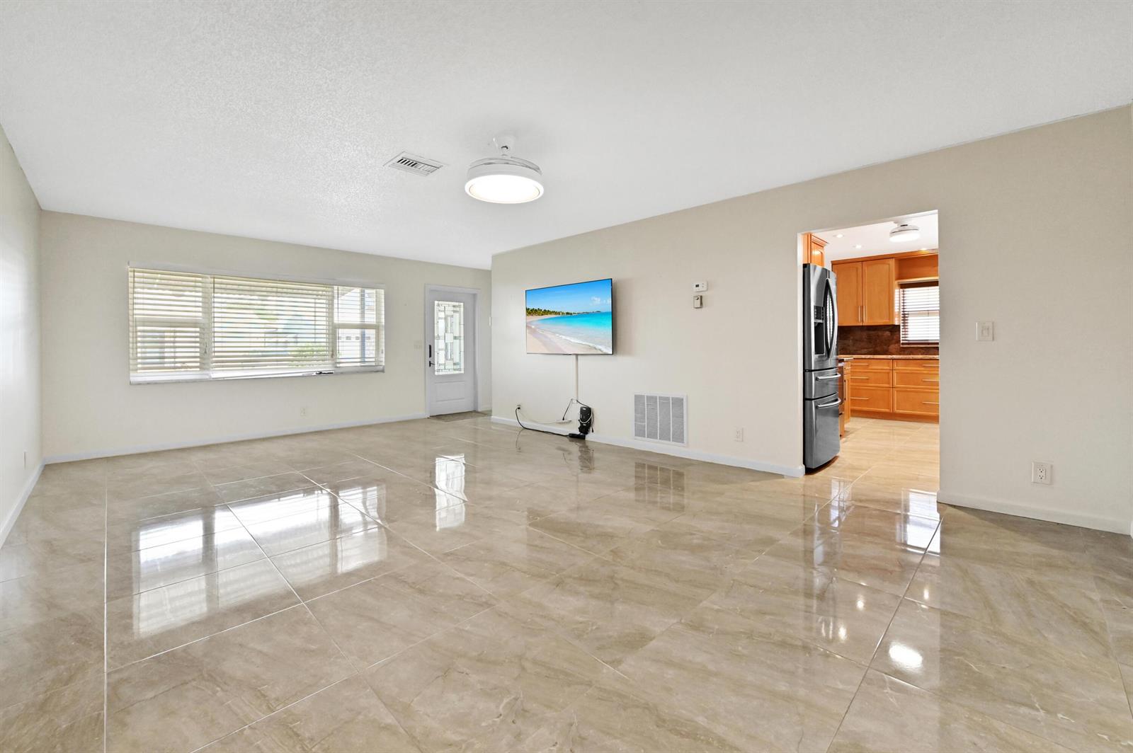A living room with beige tile flooring, a wall-mounted television, and an adjacent kitchen — 2012 SW 17th Avenue, Boynton Beach FL 33426, BOYNTON BEACH, FL