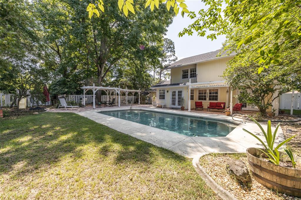A backyard features a rectangular swimming pool, a patio with red furniture, and a pergola — 31 WENDOVER LANE, PALM COAST, FL