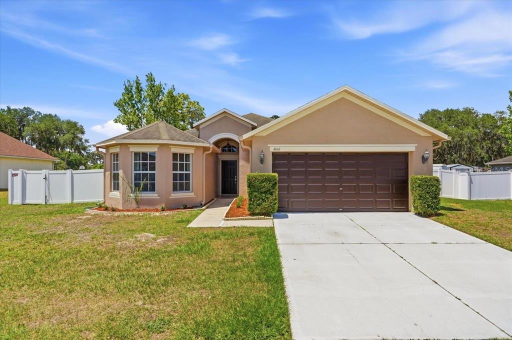 A tan single-story house with a brown garage door and a white vinyl fence — 4661 HICKORY STREAM LANE, MULBERRY, FL