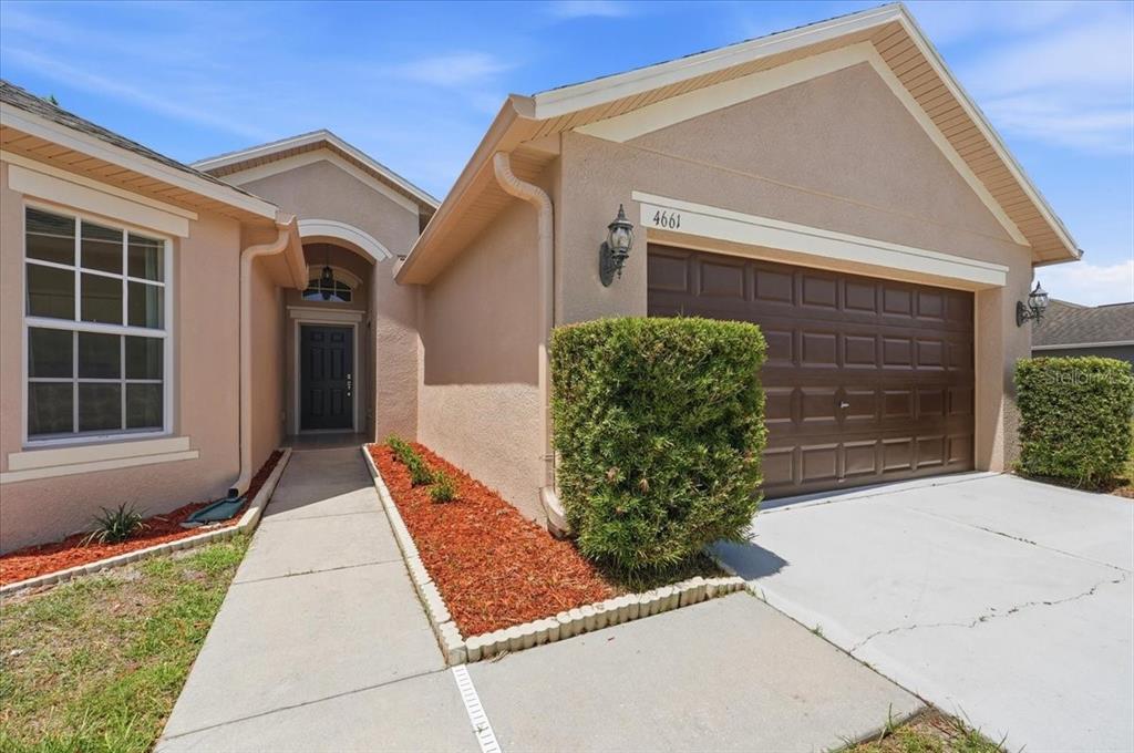 A tan stucco house features a brown garage door, a front walkway, and landscaping — 4661 HICKORY STREAM LANE, MULBERRY, FL