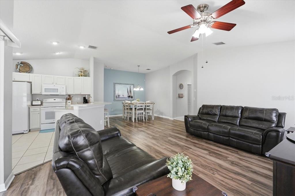 An open-concept living and dining area features wood-look flooring, white cabinetry, and leather sofas — 4661 HICKORY STREAM LANE, MULBERRY, FL