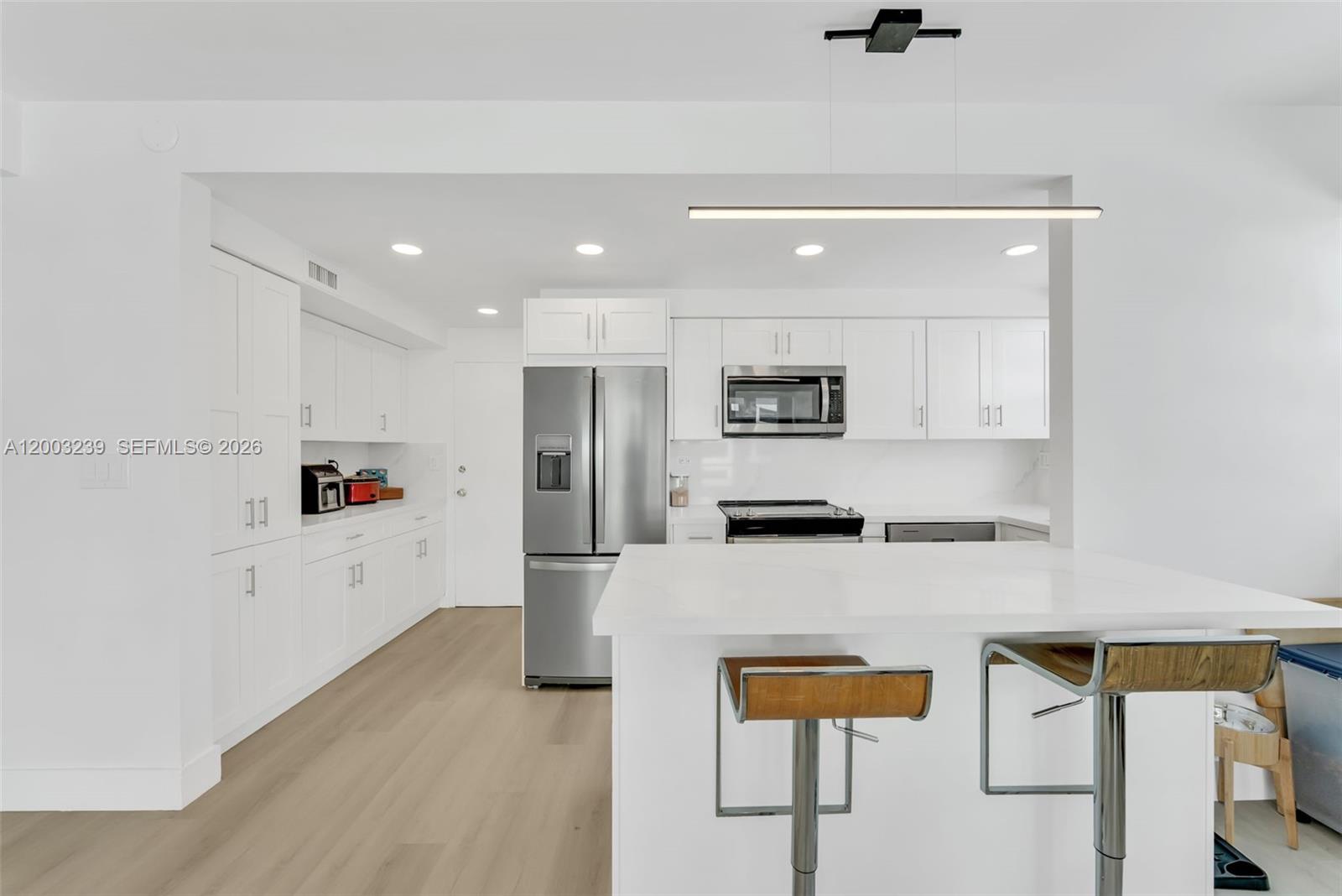 A modern white kitchen features stainless steel appliances, a center island, and light wood flooring — 1408 Brickell Bay Dr # 518, Miami FL 33131, MIAMI, FL