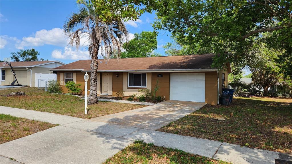 A single-story house with brown siding, a white garage door, and a palm tree — 4518 YORKSHIRE AVENUE, SPRING HILL, FL
