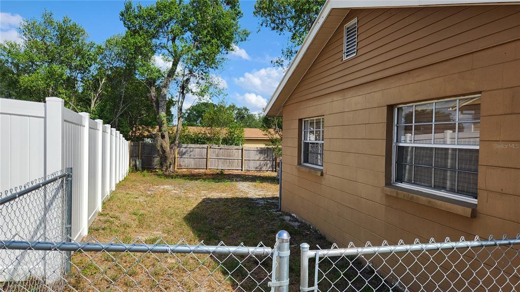 A side view of a tan house with a fenced-in yard and mature trees — 4518 YORKSHIRE AVENUE, SPRING HILL, FL