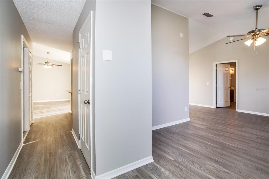 A hallway with gray wood-look flooring leads to an open living area with a ceiling fan — 24 BRADFORD COURT, KISSIMMEE, FL