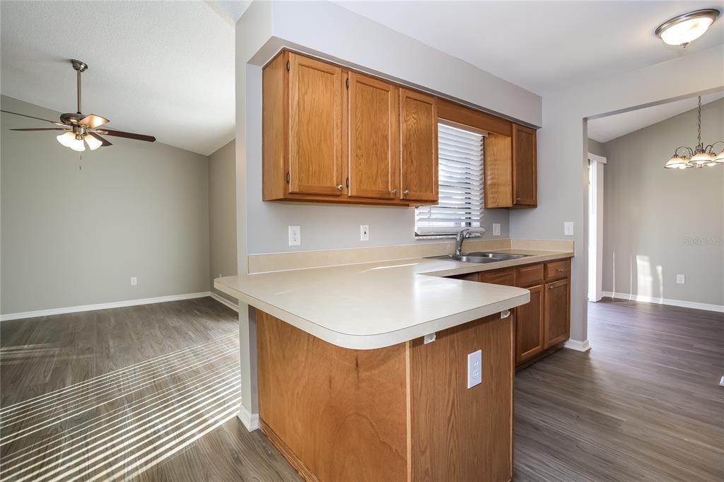 A kitchen with wood cabinets, light countertops, and wood-look flooring opens to adjacent living areas — 24 BRADFORD COURT, KISSIMMEE, FL