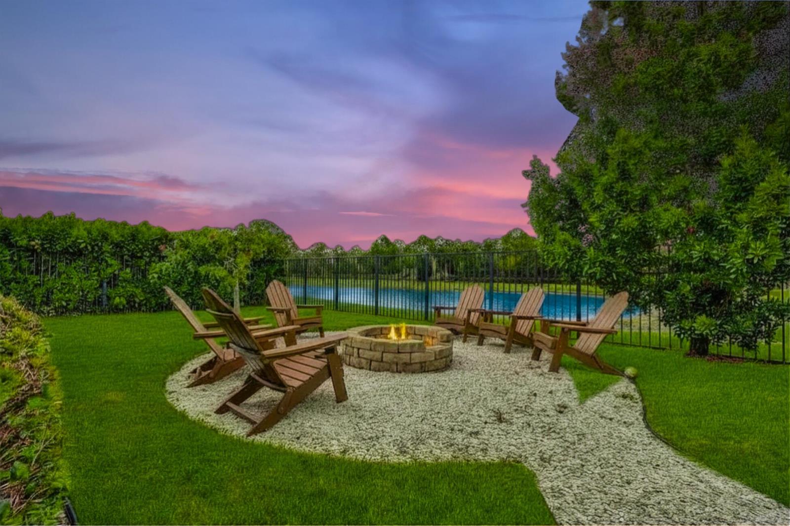 A backyard fire pit area with wooden chairs sits on a gravel patio at dusk — 15822 Orchard Drive, Westlake FL 33470, WESTLAKE, FL