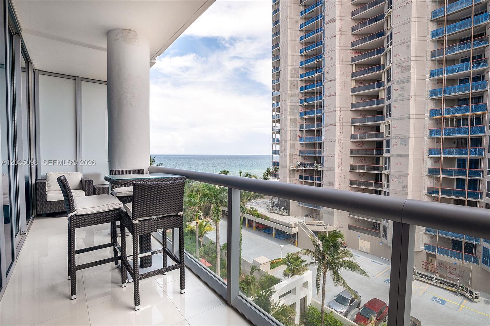 A balcony with outdoor furniture overlooks the ocean and a neighboring high-rise building under construction — 6799 Collins Ave # 510, Miami Beach FL 33141, MIAMI BEACH, FL