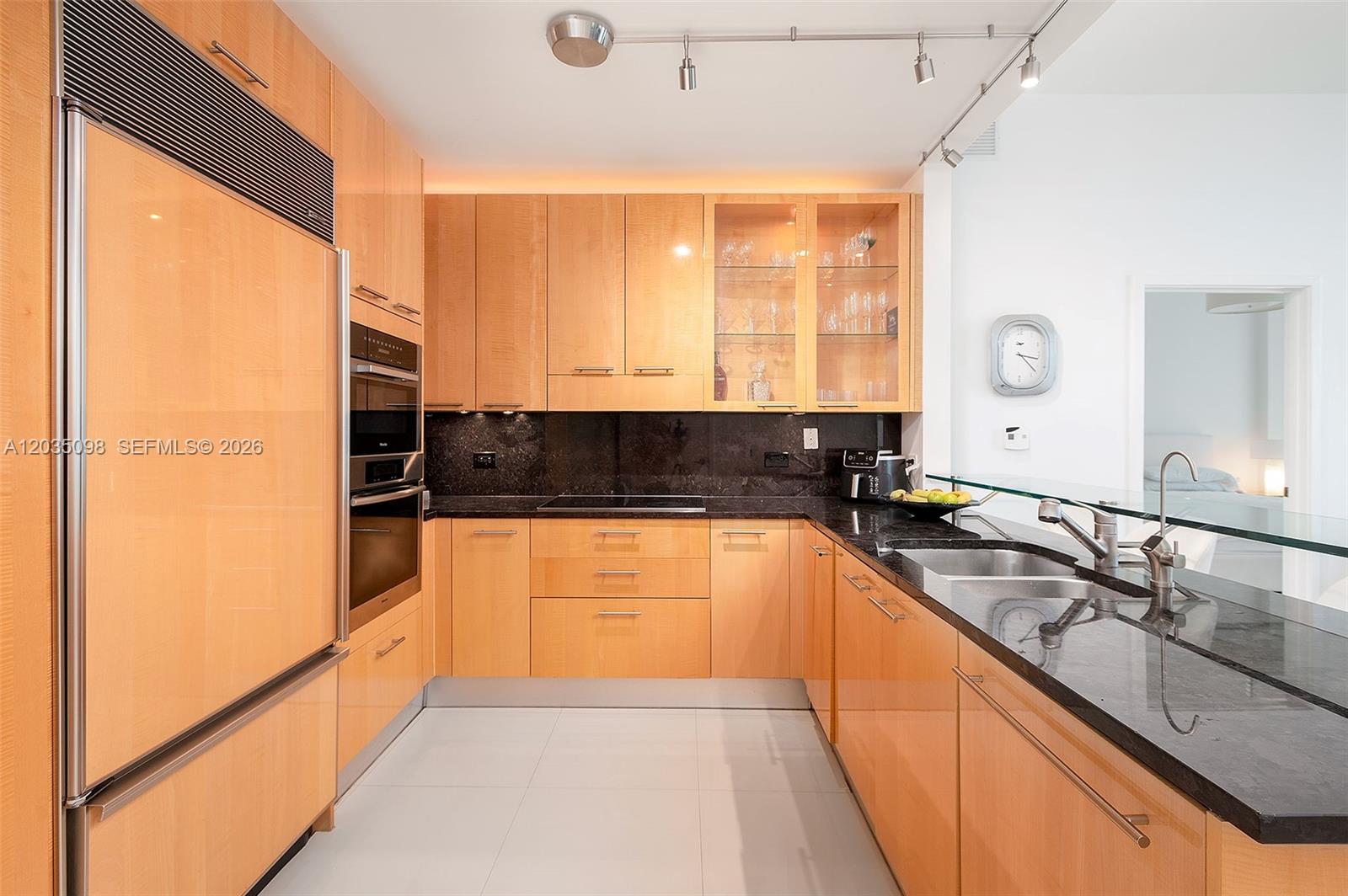 A modern kitchen features light wood cabinets, black granite countertops, and stainless steel appliances — 6799 Collins Ave # 510, Miami Beach FL 33141, MIAMI BEACH, FL