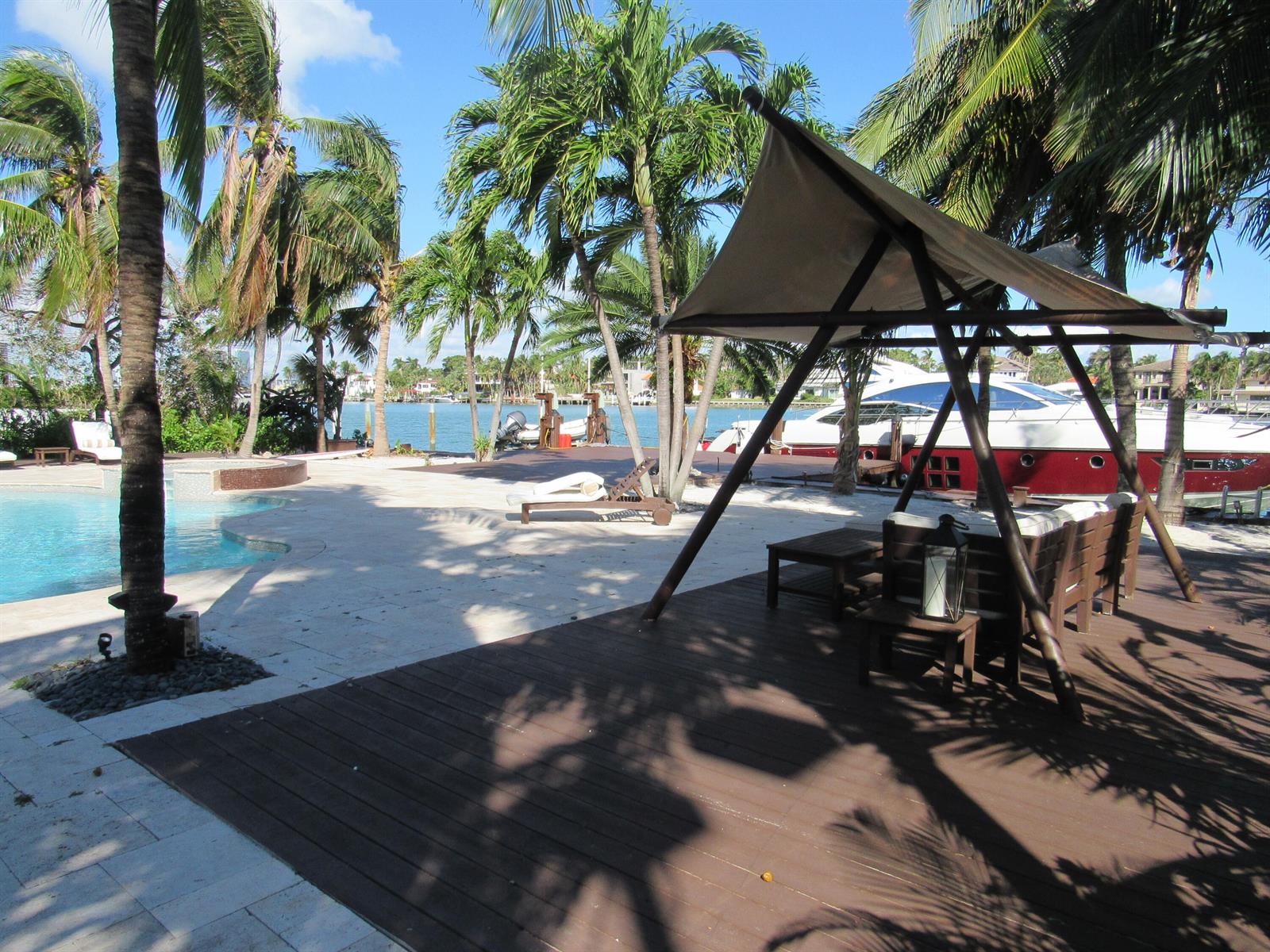 A backyard patio features a swimming pool, wooden deck, shaded seating area, and a docked yacht — 185 Palm Avenue, Miami Beach FL 33139, MIAMI BEACH, FL