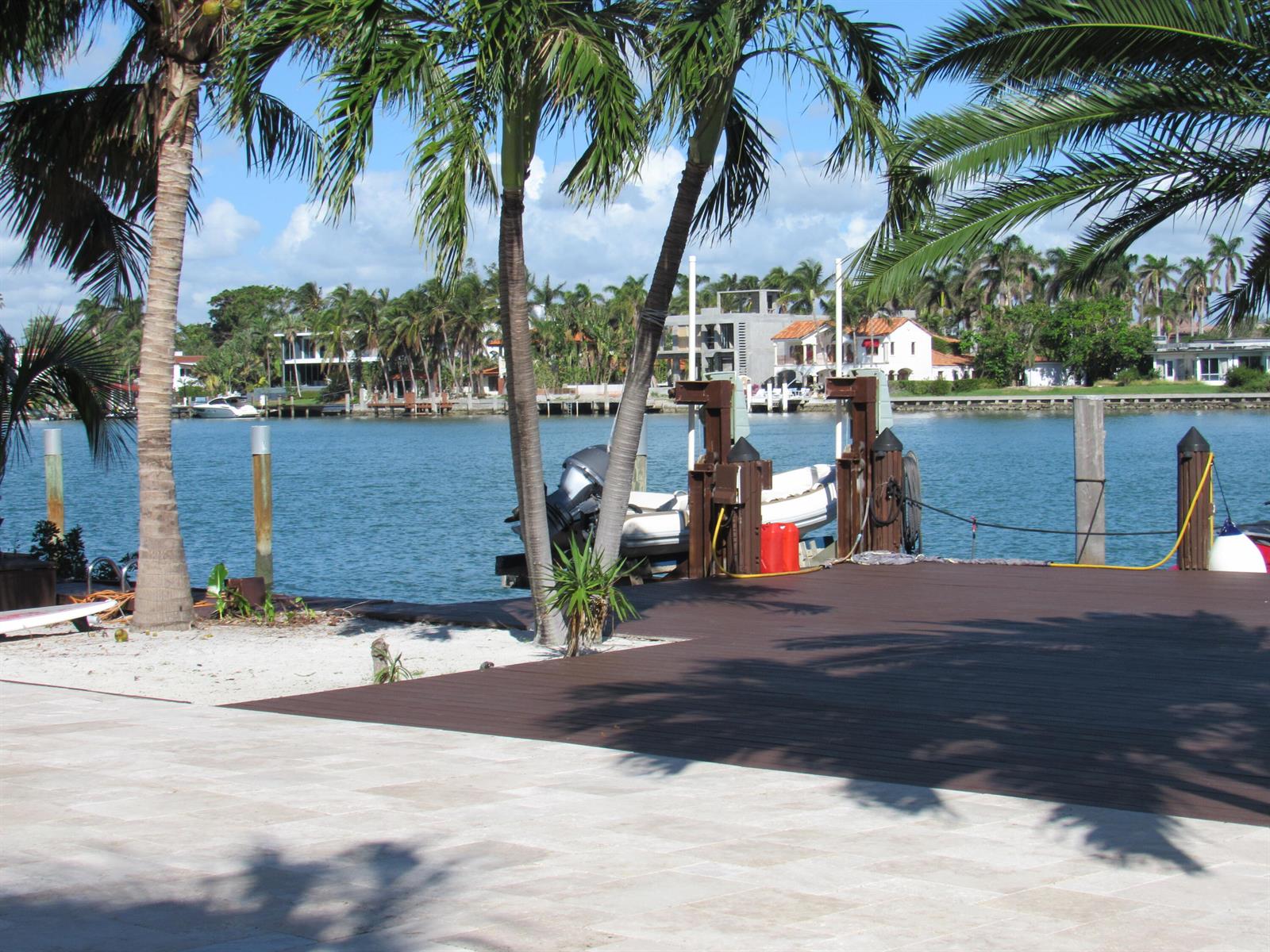 A wooden dock with a boat lift sits beside palm trees overlooking a calm canal — 185 Palm Avenue, Miami Beach FL 33139, MIAMI BEACH, FL