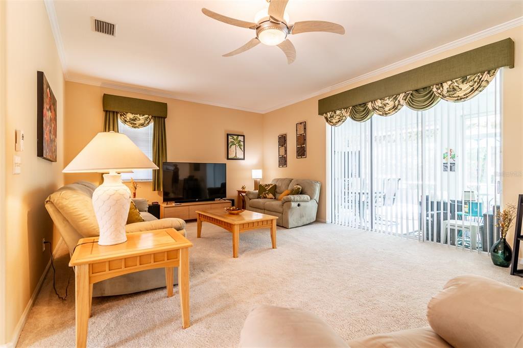 A living room features beige carpet, a ceiling fan, a television, and a sliding glass door — 2291 NW 59TH TERRACE, OCALA, FL