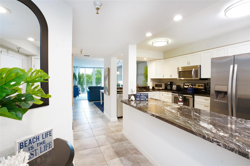 A kitchen with dark marble countertops and white cabinets opens into a living area — 19931 GULF BOULEVARD UNIT D2, INDIAN SHORES, FL
