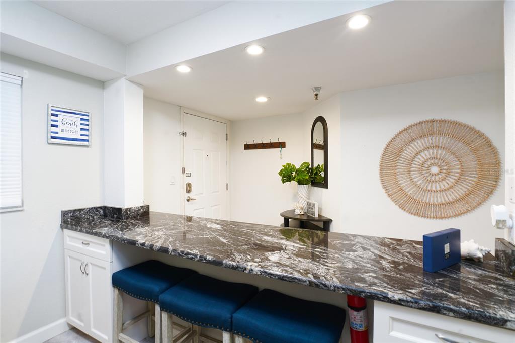 A kitchen breakfast bar features dark marble countertops, white cabinets, and three blue stools — 19931 GULF BOULEVARD UNIT D2, INDIAN SHORES, FL
