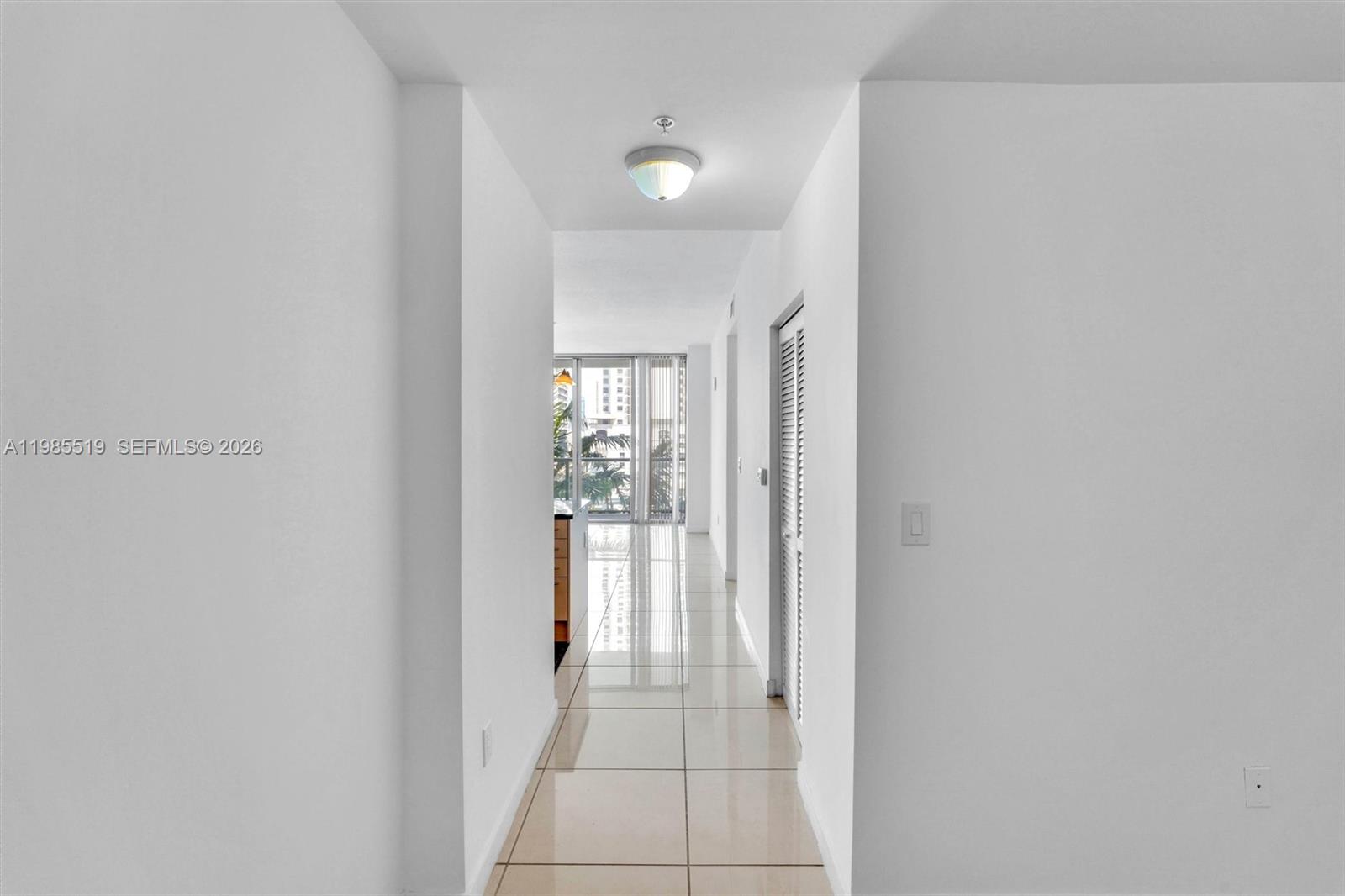 A bright hallway with white walls and light-colored tile flooring leads toward a windowed area — 79 SW 12th St # 1210, Miami FL 33130, MIAMI, FL