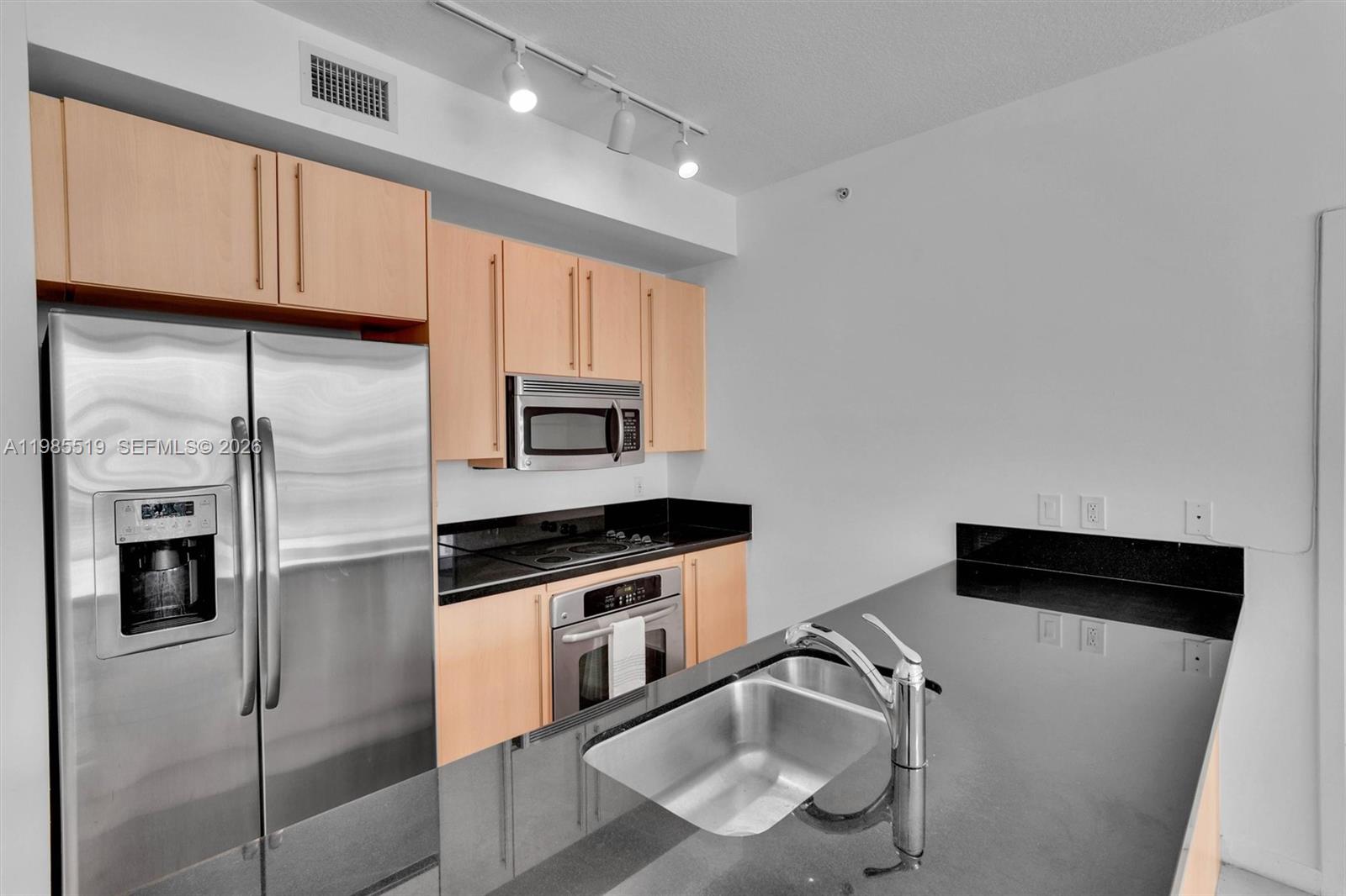 A kitchen features light wood cabinets, black countertops, stainless steel appliances, and a double sink — 79 SW 12th St # 1210, Miami FL 33130, MIAMI, FL