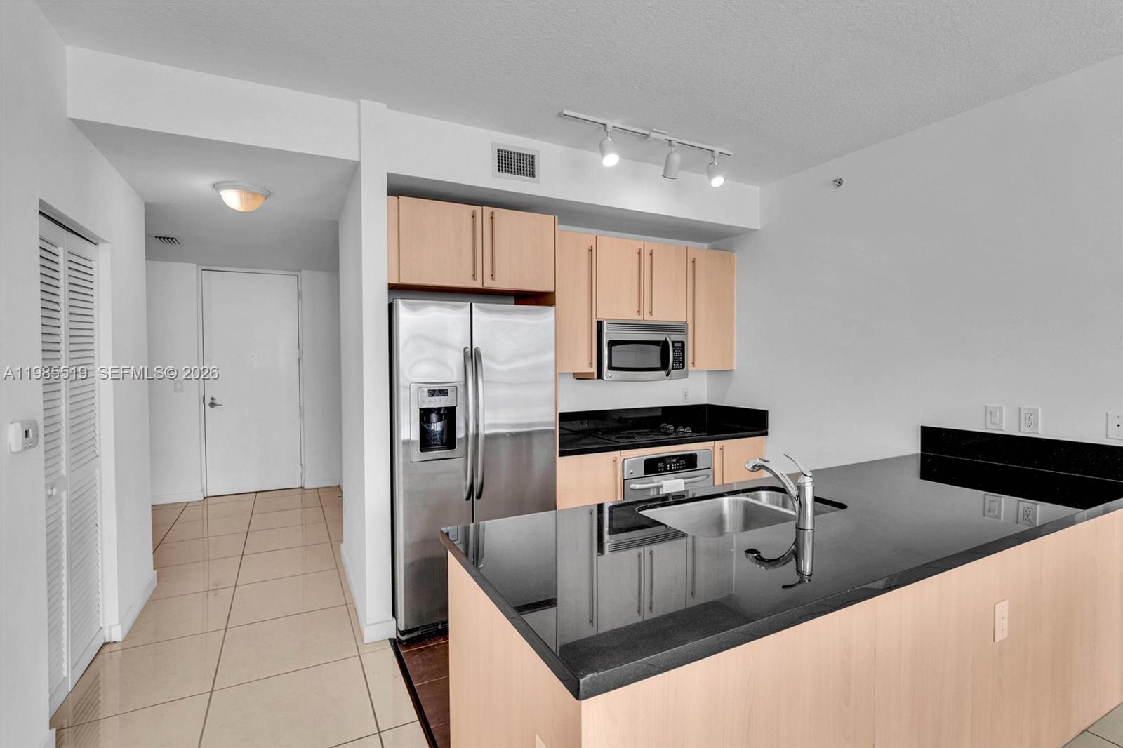 A kitchen features light wood cabinets, black countertops, stainless steel appliances, and tile flooring — 79 SW 12th St # 1210, Miami FL 33130, MIAMI, FL