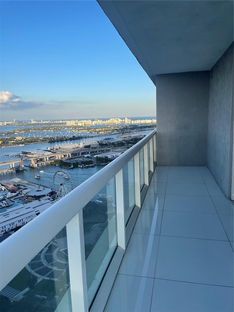 A high-rise balcony with white tile flooring overlooks a bay, city skyline, and ferris wheel — 50 Biscayne Blvd # 5001, Miami FL 33132, MIAMI, FL