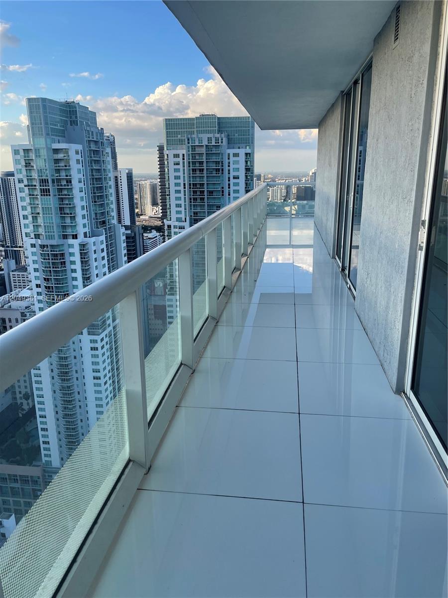 A high-rise balcony features white tile flooring, a glass railing, and views of city skyscrapers — 50 Biscayne Blvd # 5001, Miami FL 33132, MIAMI, FL