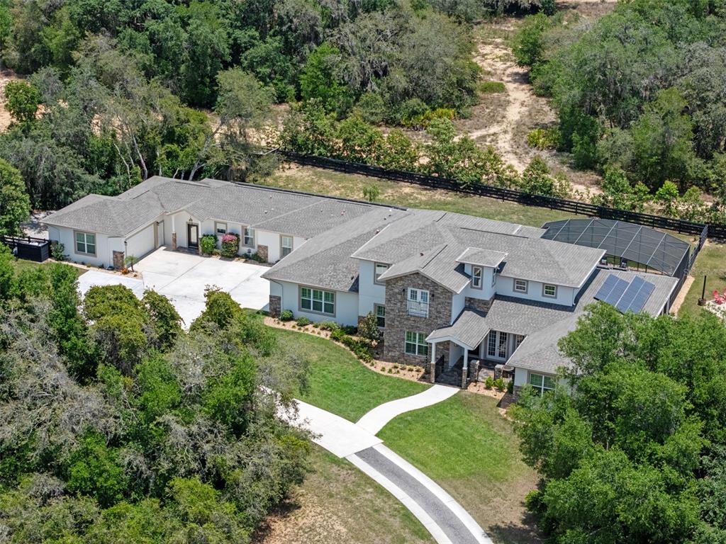 An aerial view of a large house with a stone facade, pool enclosure, and solar panels — 20199 SWEETWOOD LANE, CLERMONT, FL