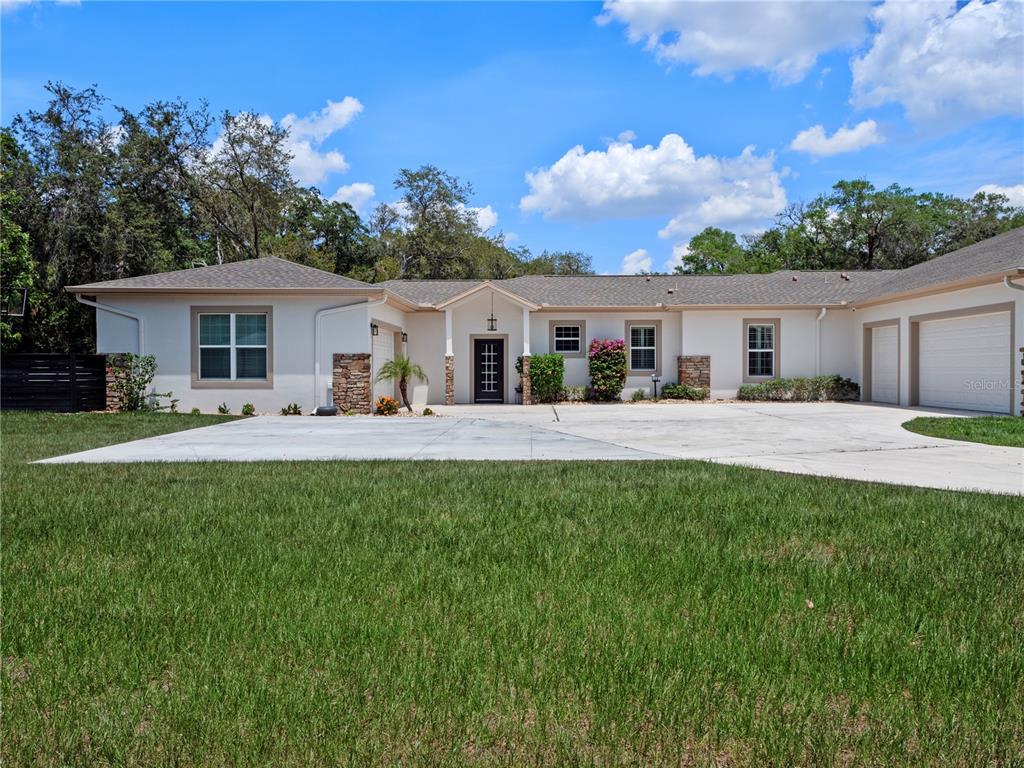 A single-story house with a white stucco exterior, stone accents, and a large concrete driveway — 20199 SWEETWOOD LANE, CLERMONT, FL