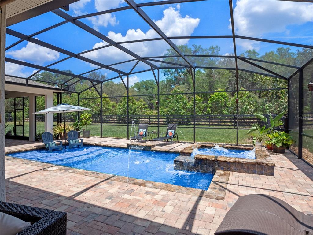 A screened-in patio features a swimming pool with a spillover spa and paver decking — 20199 SWEETWOOD LANE, CLERMONT, FL