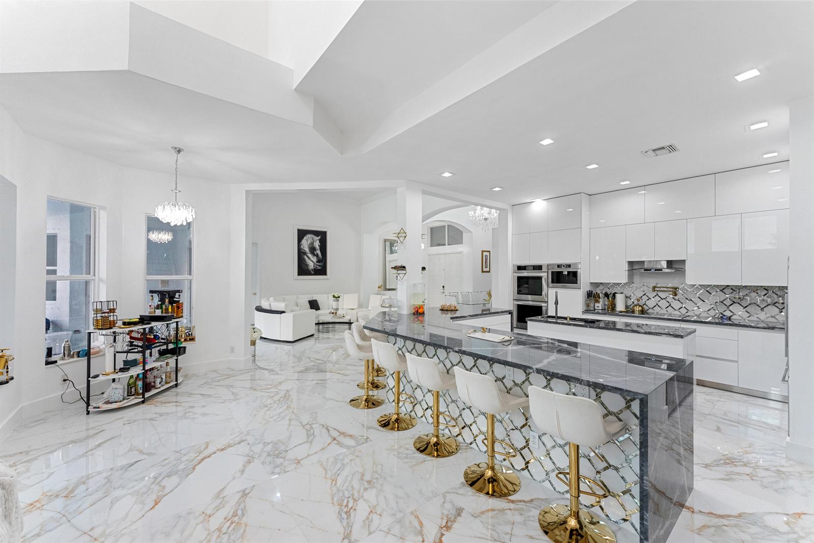 A modern kitchen features a marble-topped island with gold bar stools and white cabinetry — 11910 Osprey Point Circle, Wellington FL 33449, WELLINGTON, FL