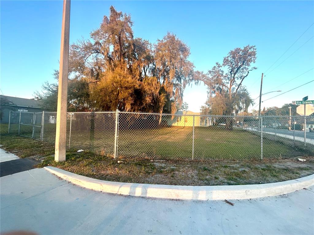 A chain-link fence surrounds a grassy lot with large trees and a street sign — 2035 S RIO GRANDE AVENUE, ORLANDO, FL