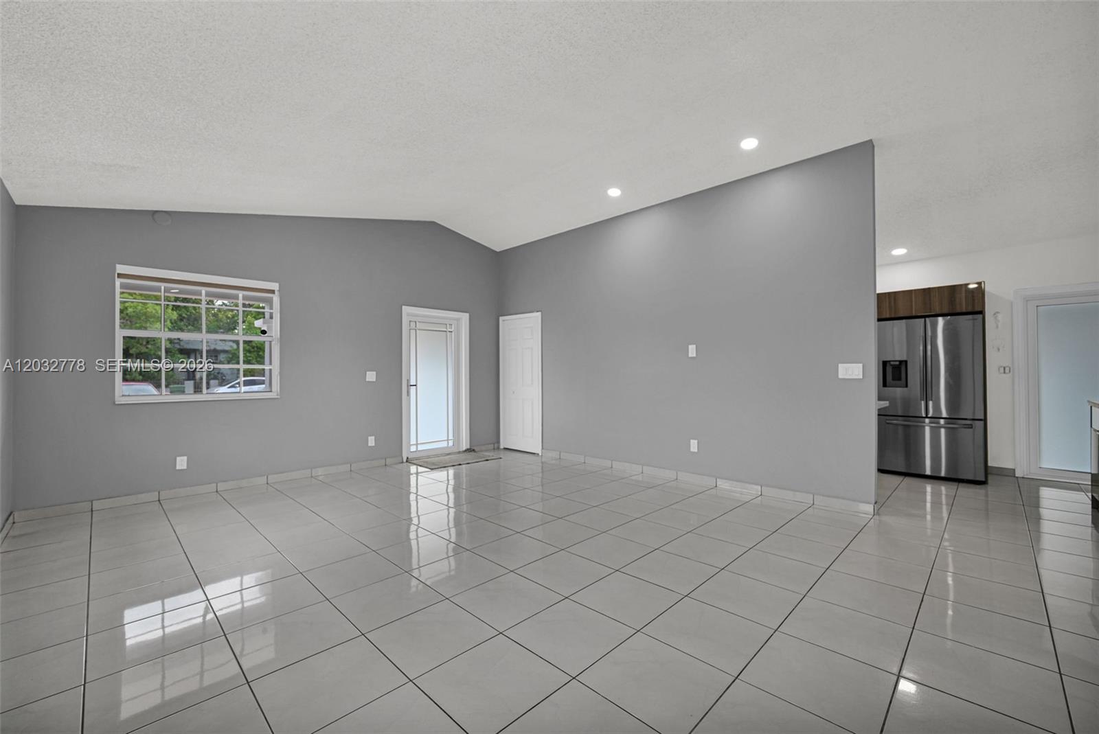 An empty living room features gray walls, white tile flooring, and a vaulted ceiling — 451 E 37th St, Hialeah FL 33013, HIALEAH, FL