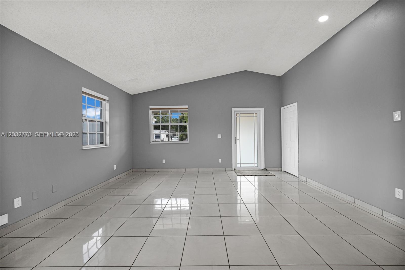 An empty room features gray walls, white tile flooring, and a vaulted ceiling — 451 E 37th St, Hialeah FL 33013, HIALEAH, FL