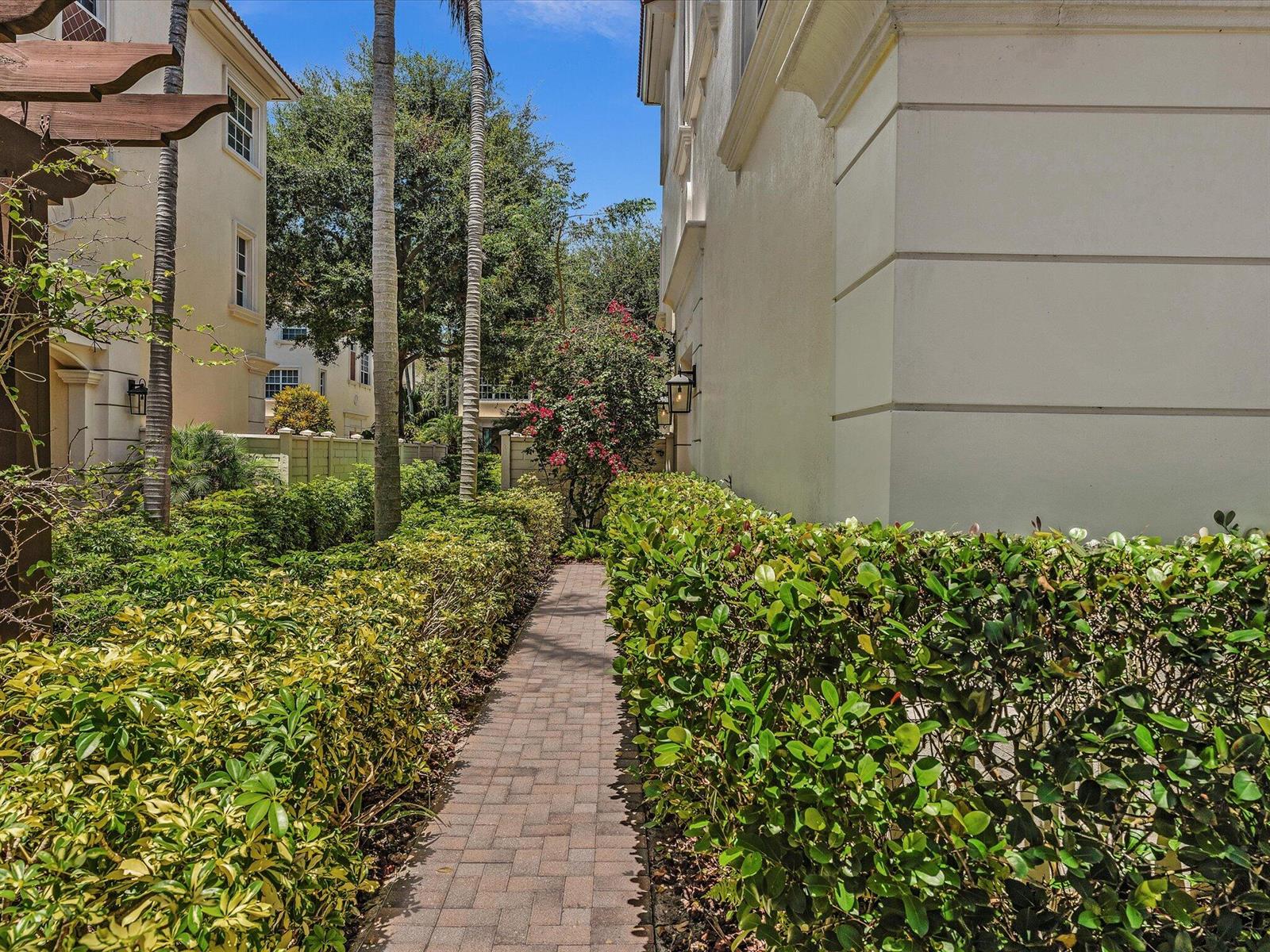 A brick walkway leads between two beige buildings lined with manicured hedges and palm trees — 5575 NE Trieste Way, Boca Raton FL 33487, BOCA RATON, FL