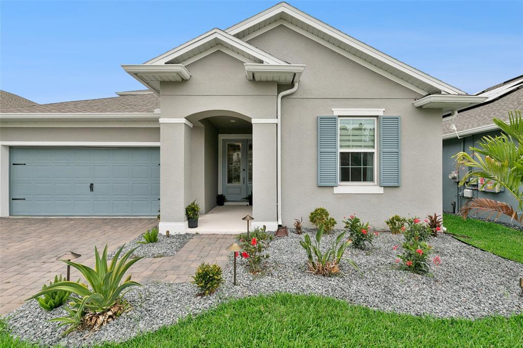 A single-story house with a gray stucco exterior, blue garage door, and a landscaped rock garden — 4465 DAVOS DRIVE, CLERMONT, FL