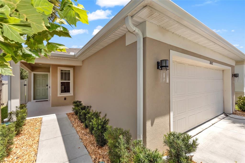 A beige house exterior features a white garage door, a green front door, and landscaping — 3082 GREEN PARK DRIVE, DELAND, FL