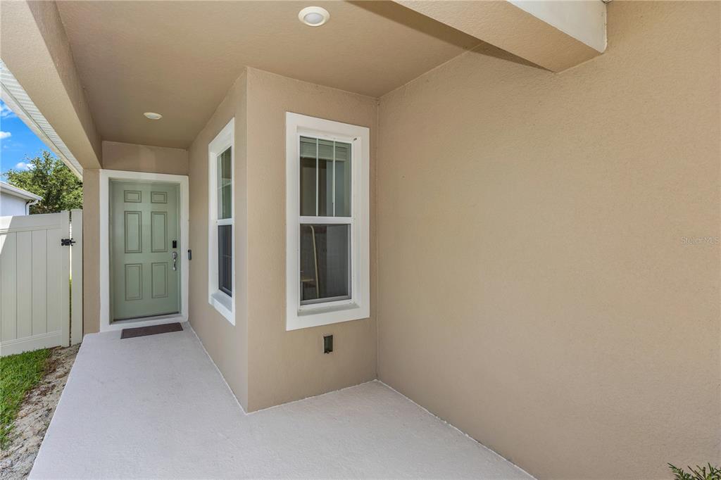 A covered concrete patio features a light green door, two windows, and beige exterior walls — 3082 GREEN PARK DRIVE, DELAND, FL