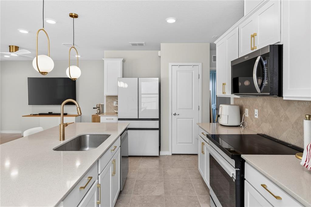 A modern kitchen features white cabinets, gold hardware, a quartz island, and stainless steel appliances — 3082 GREEN PARK DRIVE, DELAND, FL